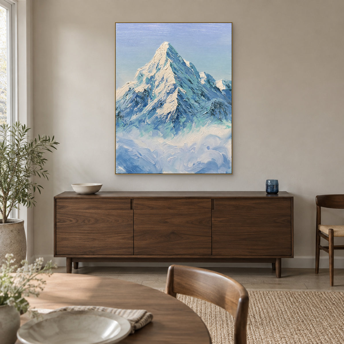 Tableau de montagne au-dessus des nuages, dans un cadre champagne au-dessus d’un buffet sombre de salle à manger.