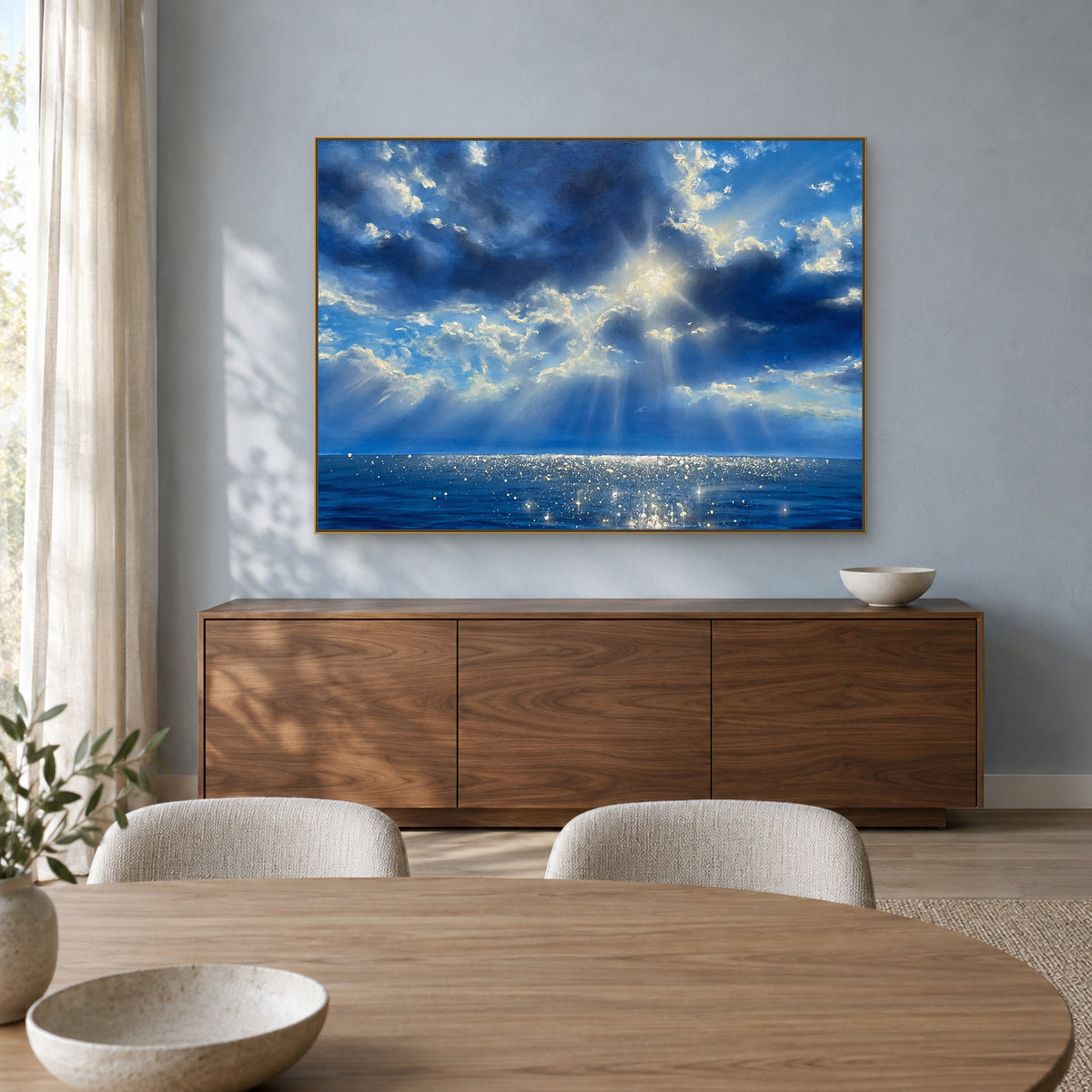 Tableau de mer et de nuages bleus dans un cadre champagne, au-dessus d’un buffet en noyer dans une salle à manger.