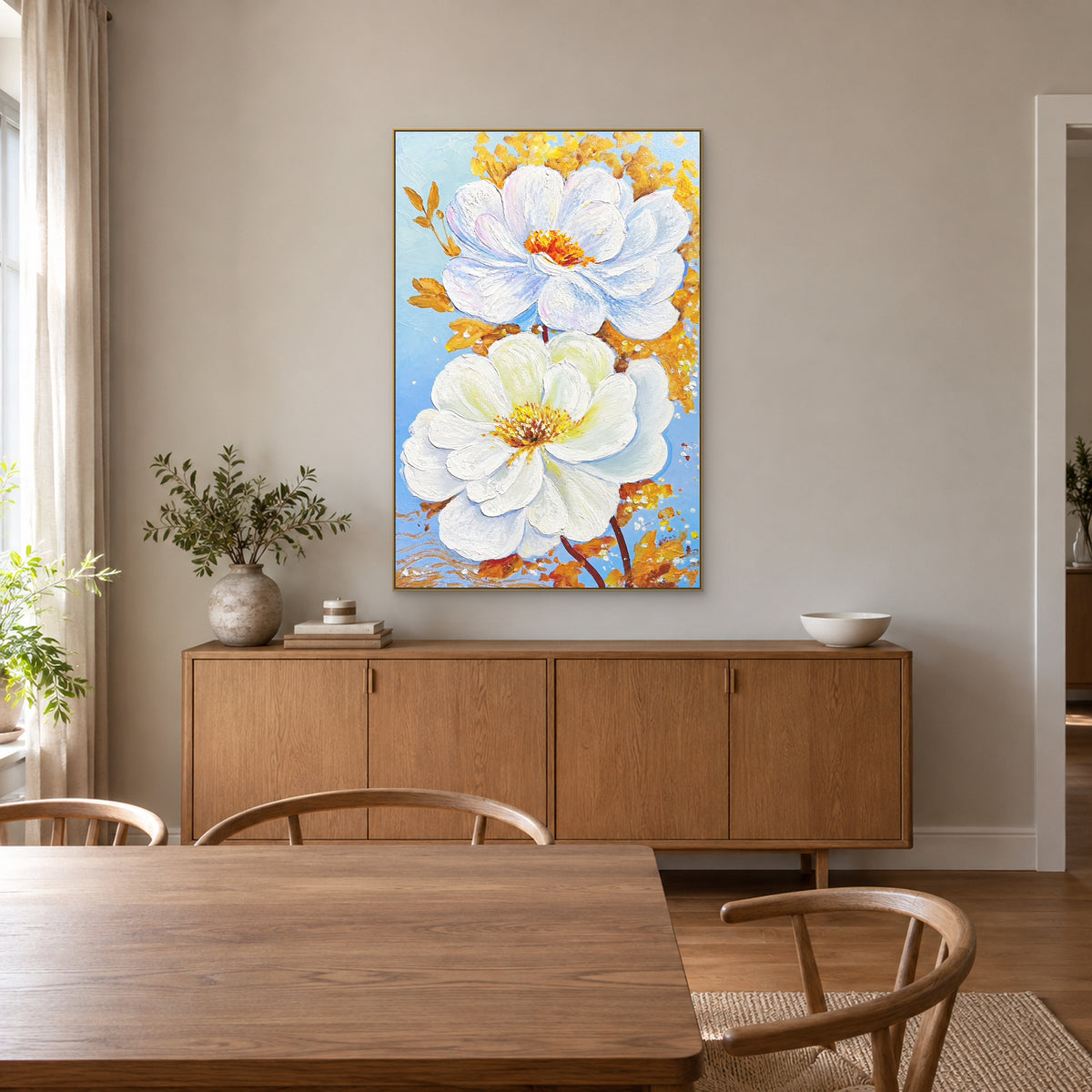 Fleurs blanches et dorées dans un cadre flottant champagne au-dessus d’un buffet en bois, dans une salle à manger lumineuse.