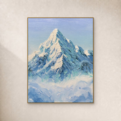 Ivory snow peak and blue-green ridges above clouds, in a slim gold frame on a warm ivory wall.