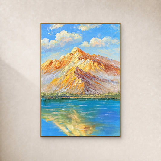 Amber mountain ridges and their blue-lake reflection in a thin gold-tone floating frame on an ivory wall