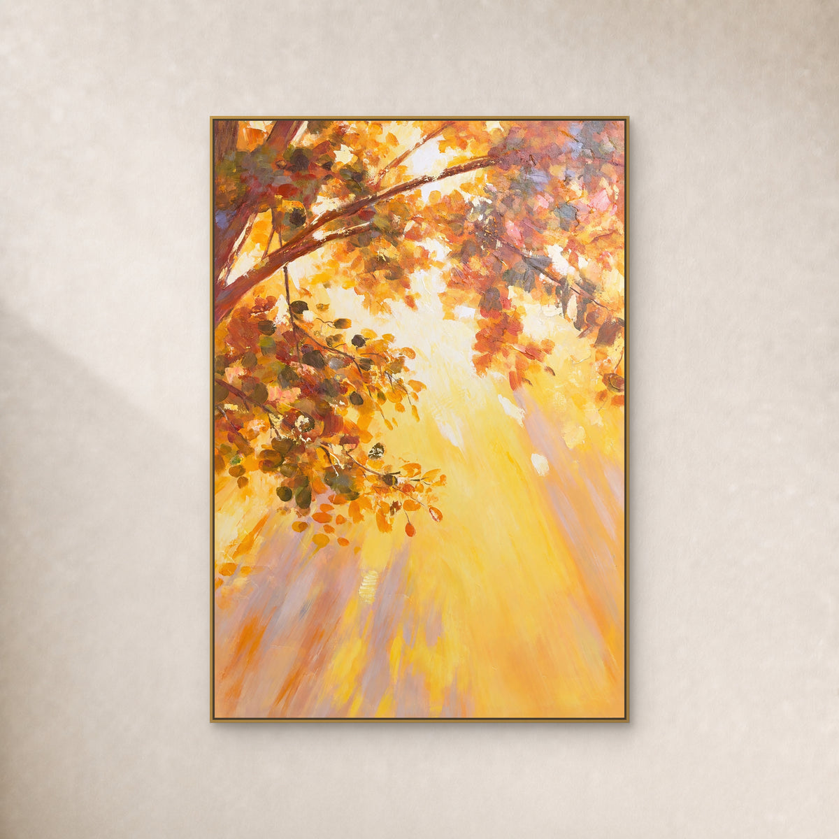 Tableau vertical de feuilles automnales ambrées et de lumière dorée, dans un fin cadre flottant doré sur un mur ivoire.