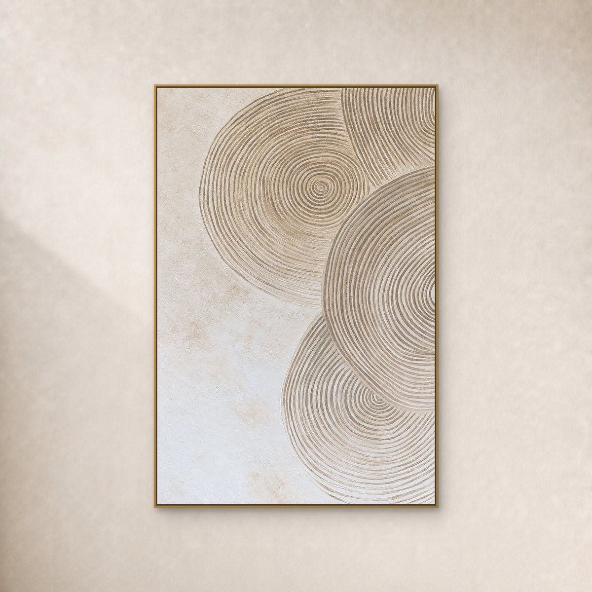 Overlapping sand-coloured concentric rings on an ivory textured ground, in a slim gold frame on a plain ivory wall.