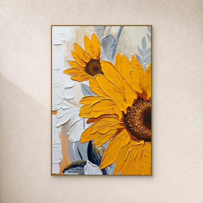 Two yellow sunflowers with raised petals and blue-grey leaves in a slim gold-tone frame on an ivory wall