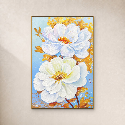 Deux fleurs blanches et un feuillage doré sur fond bleu pâle, dans un fin cadre flottant doré sur un mur ivoire.