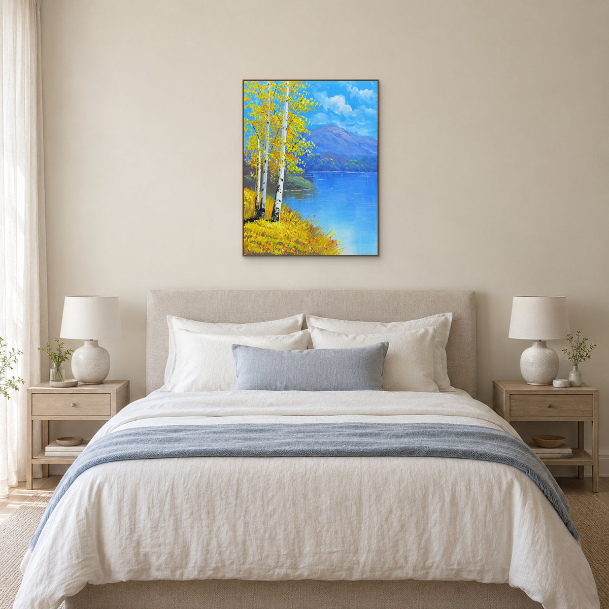 Tableau de bouleaux jaunes et de lac bleu dans un cadre ton chêne, centré au-dessus d’un lit capitonné crème.