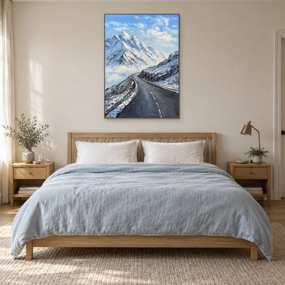 Tableau vertical de montagne enneigée, cadre flottant ton chêne, centré au-dessus d’un lit au linge bleu pâle