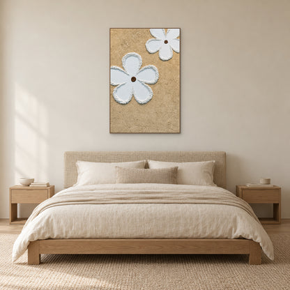 Fleurs blanches en relief dans un cadre ton chêne, au-dessus d’une tête de lit tissée et de linge crème