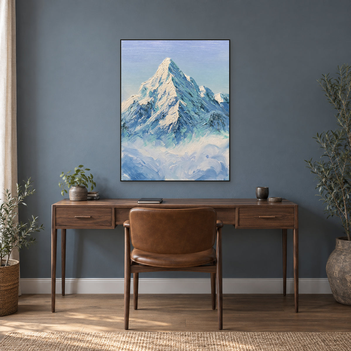 Snow peak and curling cloud painting in a thin black frame, above a walnut-coloured desk on a blue-grey wall.