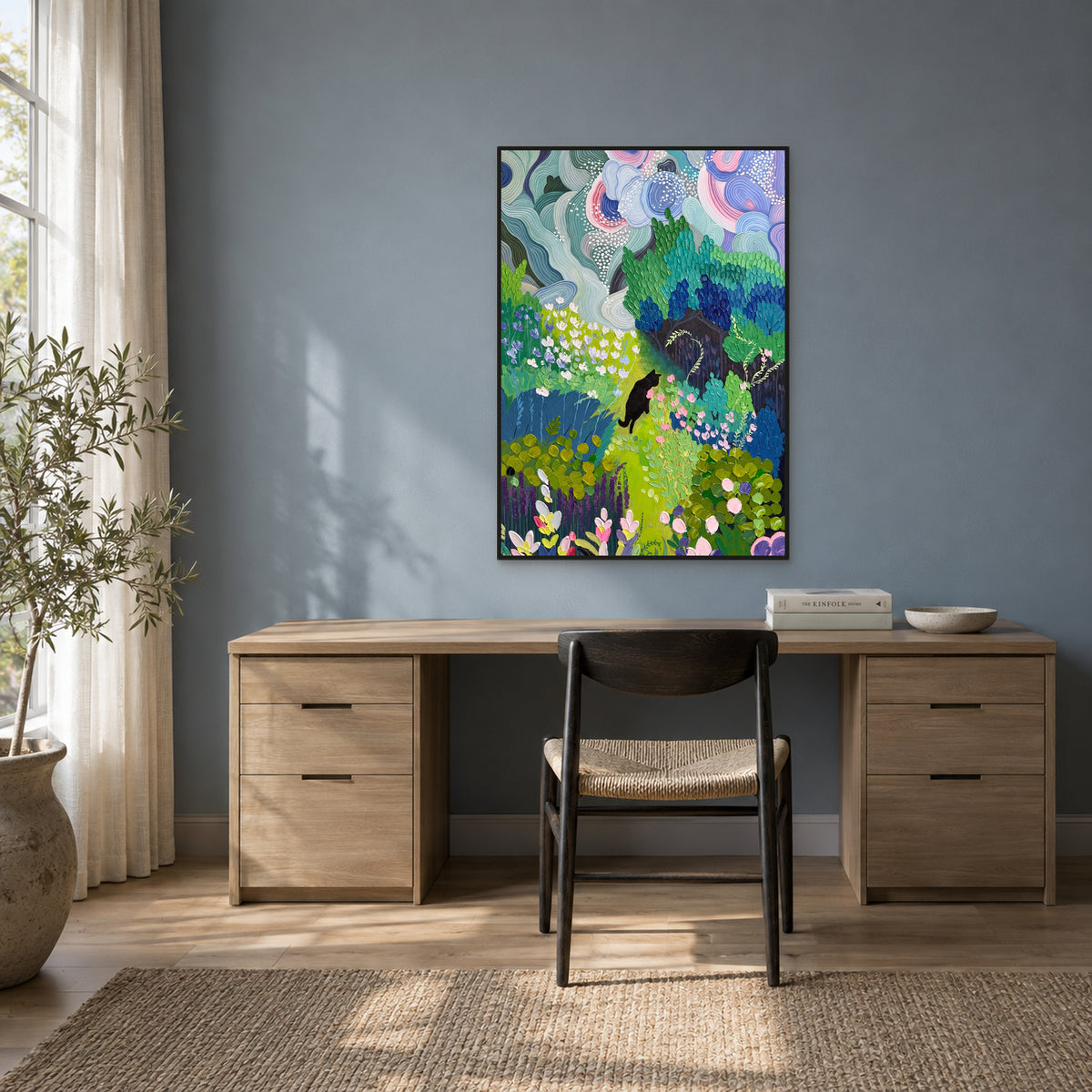 Black cat and blue-green garden painting in a black floating frame above a wood desk on a blue-grey wall