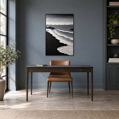 Tableau marin vertical au sable noir dans un cadre flottant noir, au-dessus d’un bureau en bois foncé et d’une chaise fauve contre un mur gris ardoise