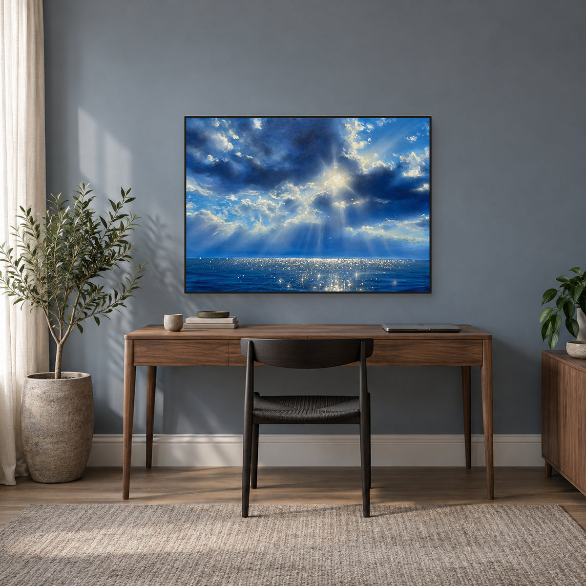 Tableau de mer bleue éclairée par le soleil, dans un fin cadre noir au-dessus d’un bureau en noyer, sur un mur bleu-gris.