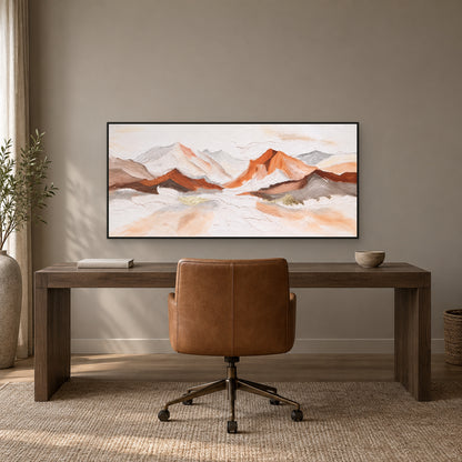 Copper and ivory mountain painting in a black floating frame above a dark wooden desk and caramel chair