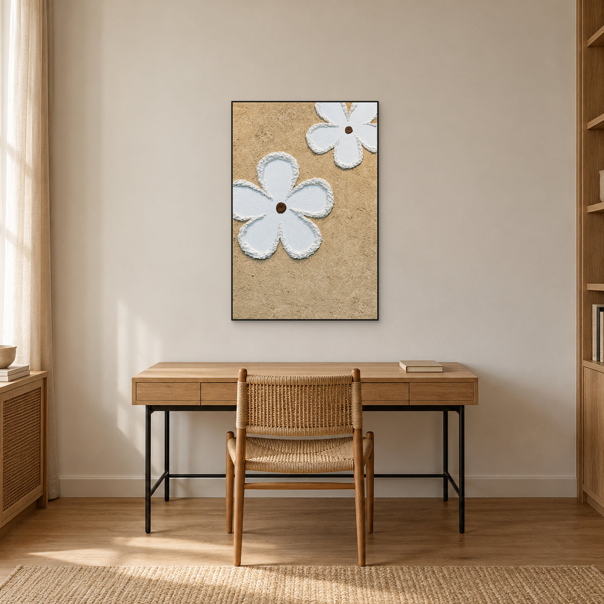 Tableau de fleurs blanc et beige à fin cadre noir, au-dessus d’un bureau en bois clair et d’une chaise tissée