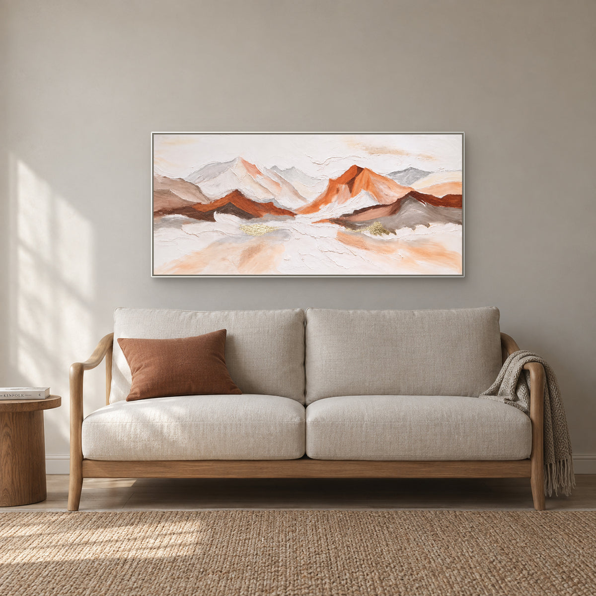 Textured mountain panorama in a white floating frame above an ivory reading sofa with a terracotta cushion