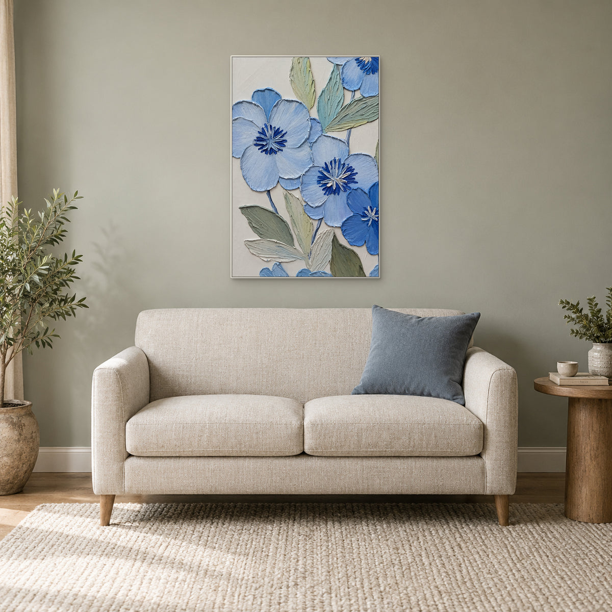 Tableau floral bleu au cadre blanc au-dessus d'un petit canapé crème, près d'une plante dans un coin lecture