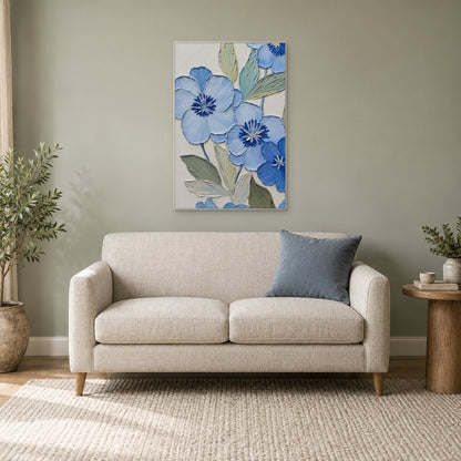Tableau floral bleu au cadre blanc au-dessus d'un petit canapé crème, près d'une plante dans un coin lecture