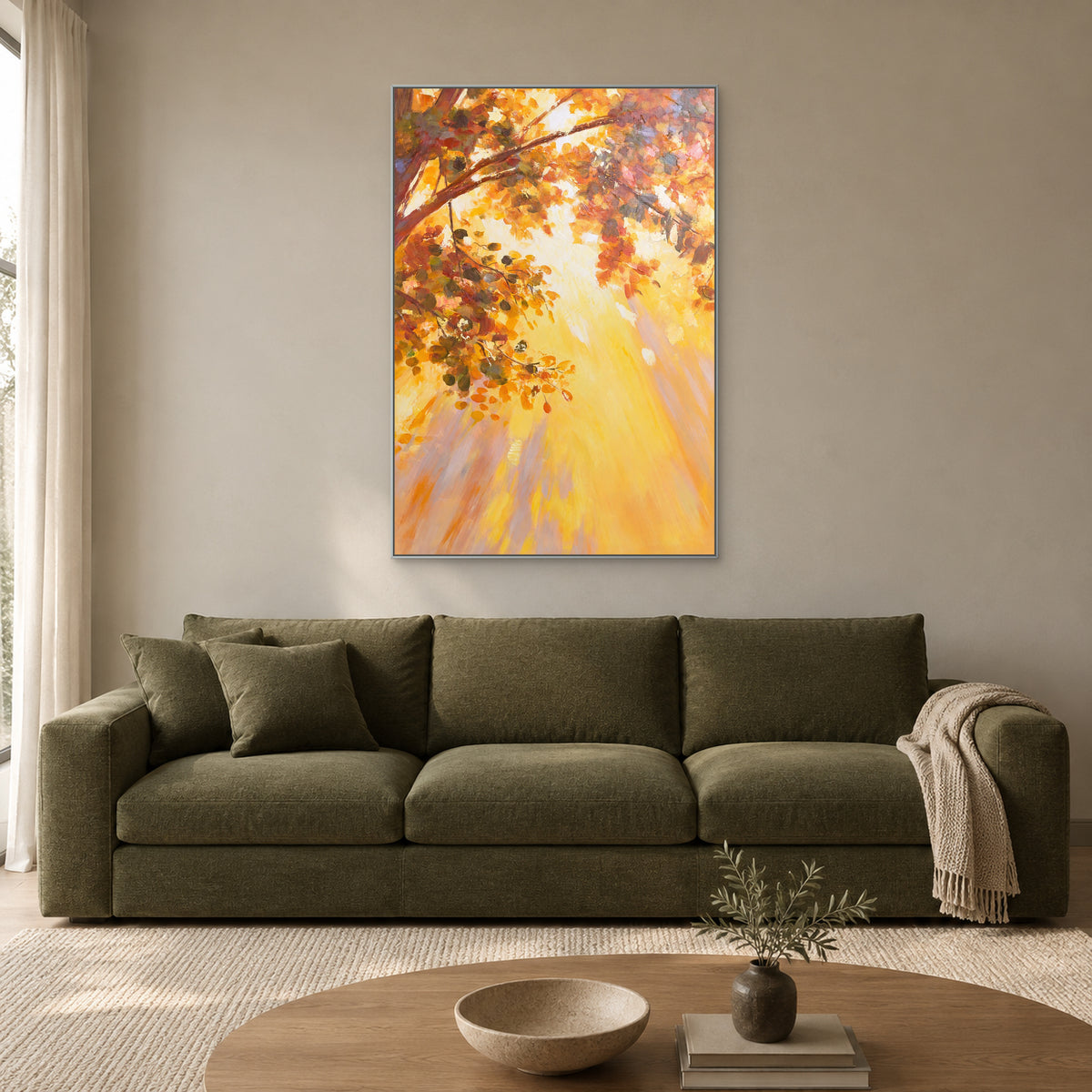 Tableau d’arbre automnal aux tons chauds dans un fin cadre argenté, au-dessus d’un canapé olive dans un salon lumineux.