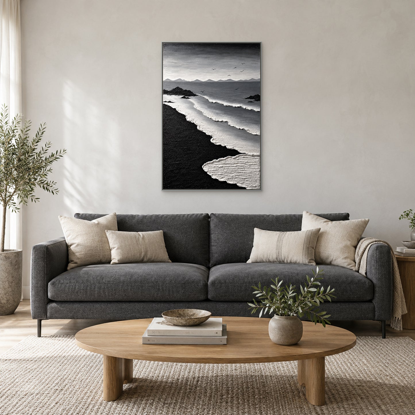 Tableau côtier monochrome dans un cadre flottant argenté, centré au-dessus d’un canapé anthracite avec coussins ivoire et table basse ovale en bois