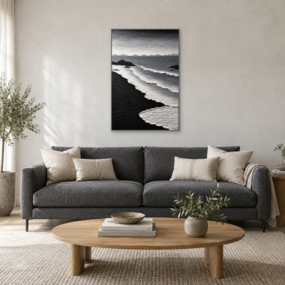 Tableau côtier monochrome dans un cadre flottant argenté, centré au-dessus d’un canapé anthracite avec coussins ivoire et table basse ovale en bois