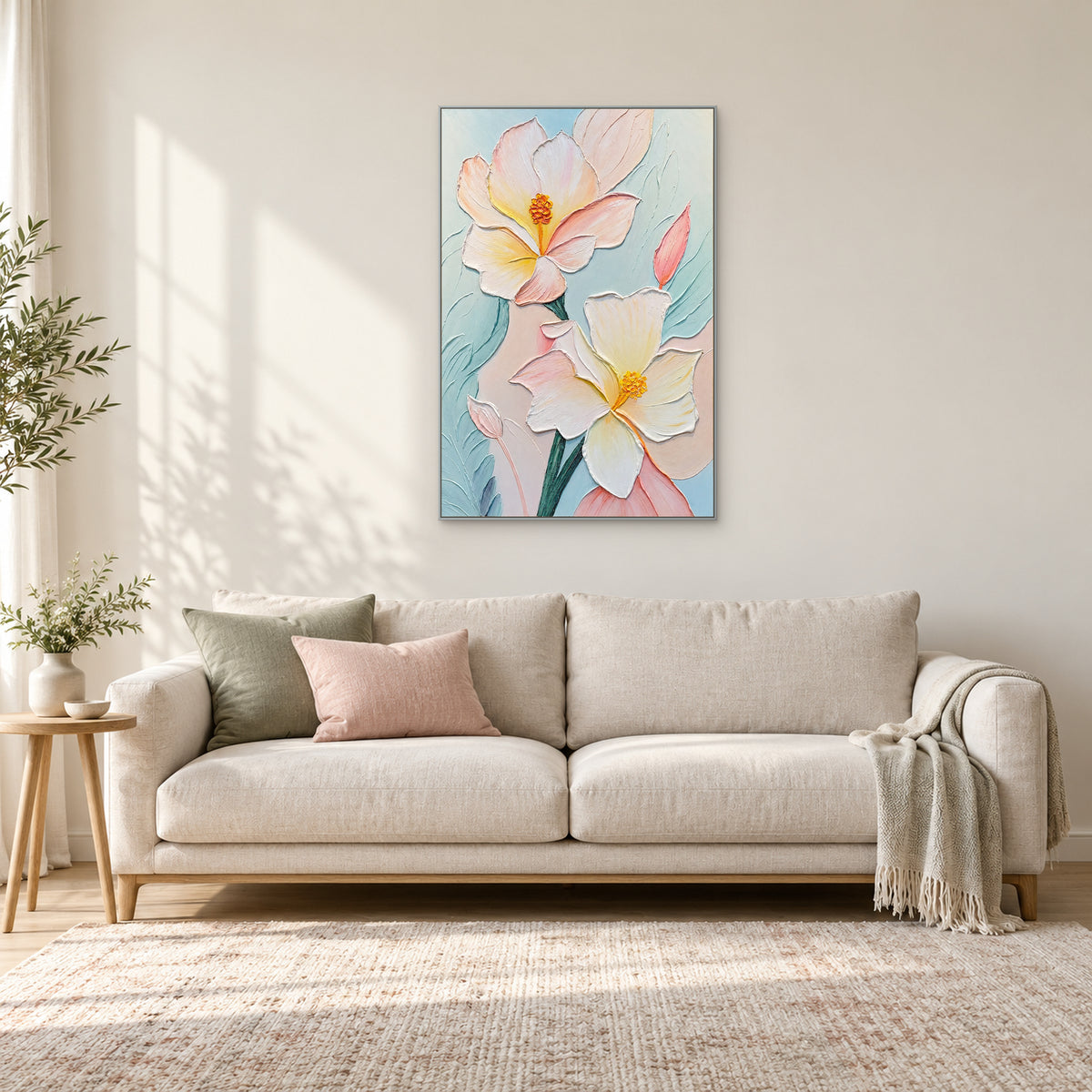 Pastel floral painting in a thin silver-coloured frame centred above a cream sofa with pink and green cushions