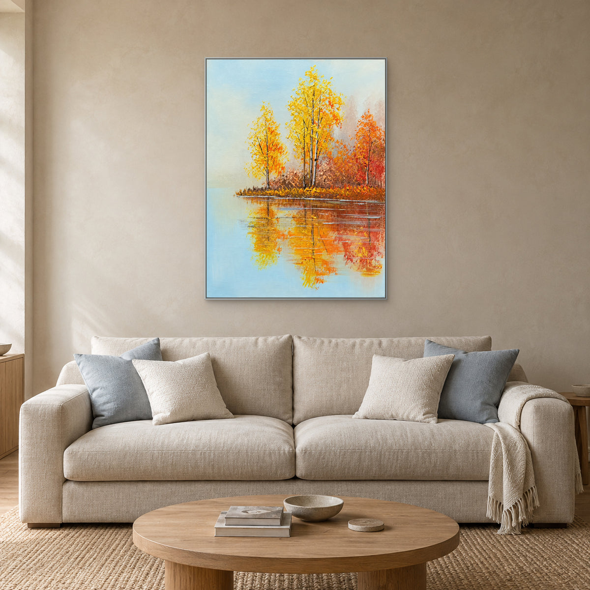 Tableau vertical de bouleaux dorés au bord d’un lac, cadre argenté, au-dessus d’un canapé beige aux coussins bleu-gris