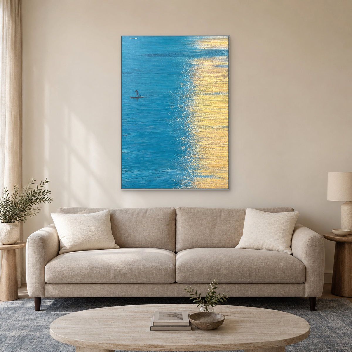 Tableau d’eau turquoise et de reflets dorés, cadre argenté au-dessus d’un canapé taupe clair