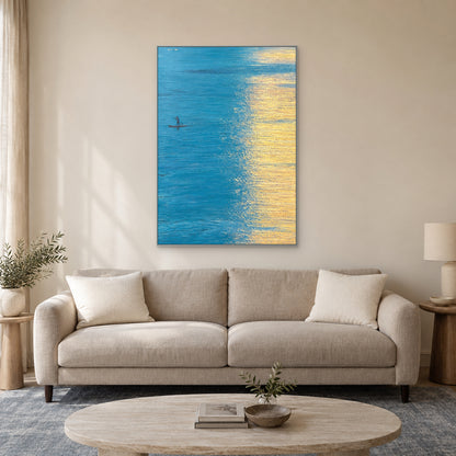 Tableau d’eau turquoise et de reflets dorés, cadre argenté au-dessus d’un canapé taupe clair