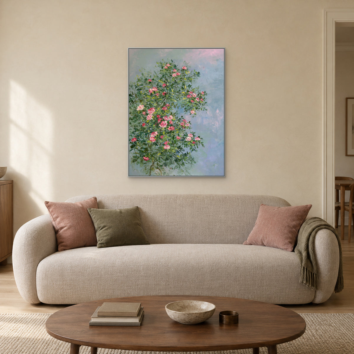 Pink rose and green foliage painting in a thin silver-tone frame centred above a light sofa