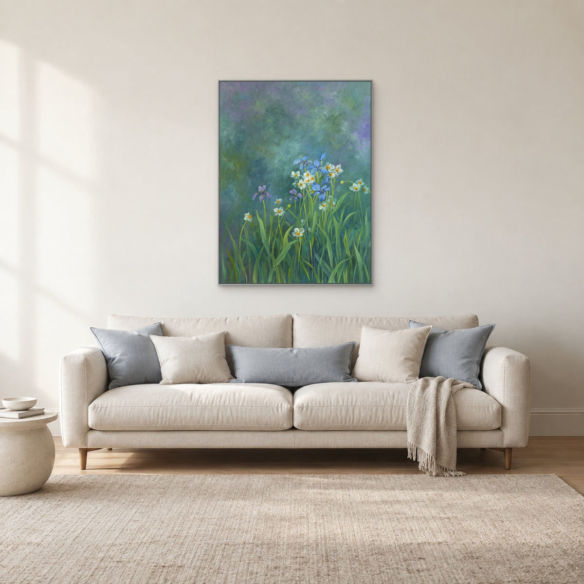 Tableau floral vert bleuté dans un cadre argenté, au-dessus d’un canapé crème aux coussins bleu pâle