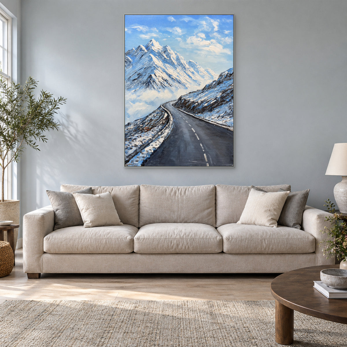 Sommets enneigés et route sinueuse, cadre flottant argenté, au-dessus d’un canapé crème sur un mur bleu-gris