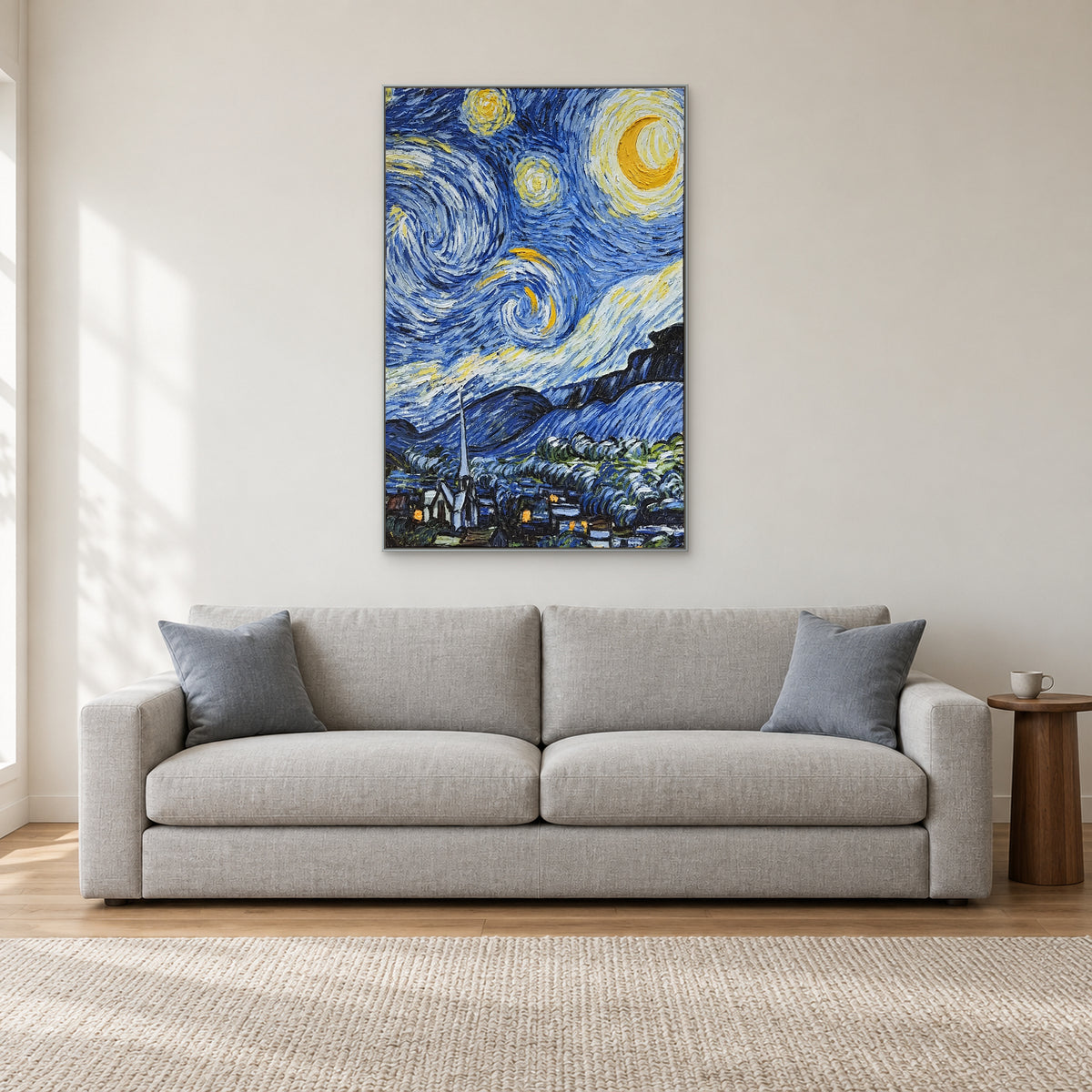 Tableau vertical de village au clair de lune dans un cadre argenté, centré au-dessus d’un canapé gris.