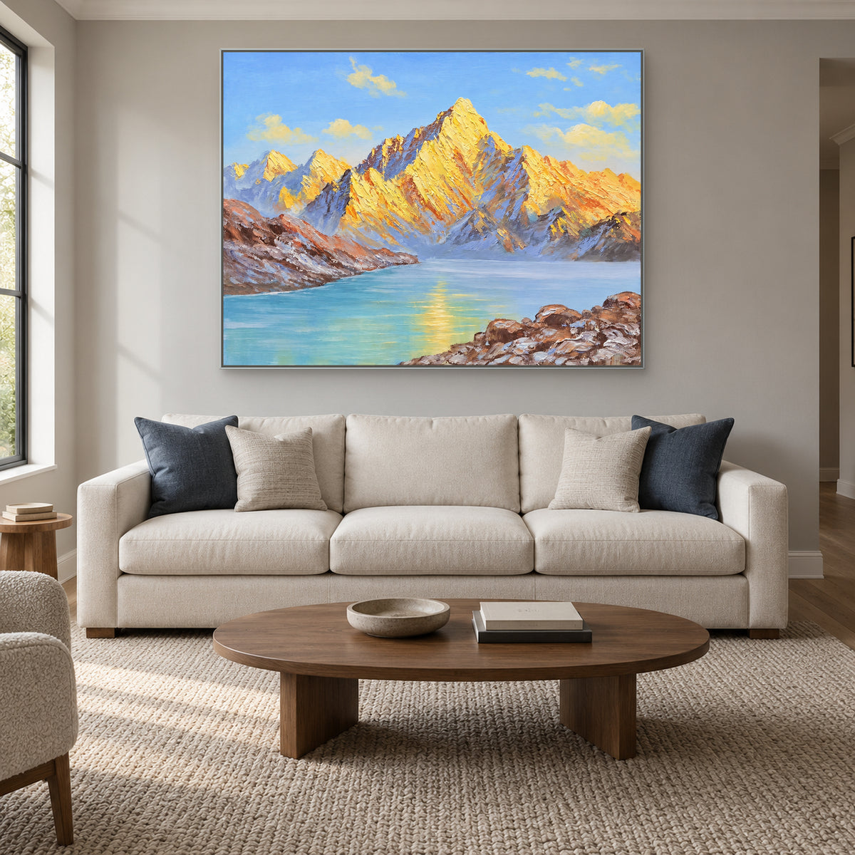 Horizontal golden mountain painting in a silver-tone frame above a cream sofa with blue cushions