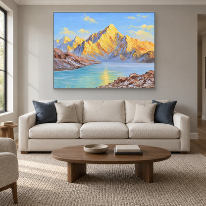 Horizontal golden mountain painting in a silver-tone frame above a cream sofa with blue cushions