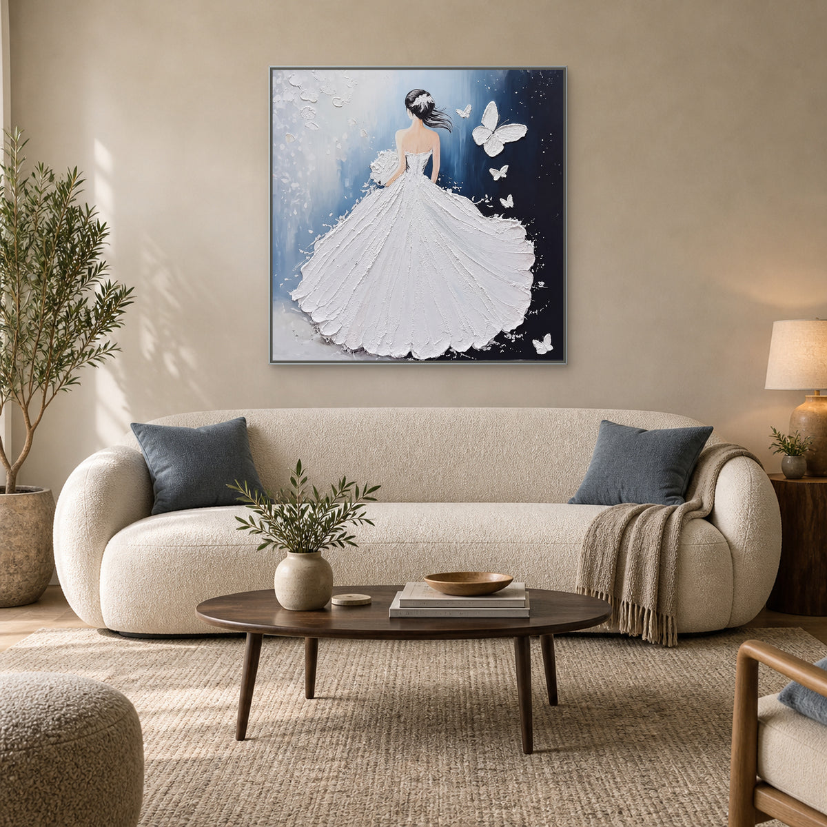Tableau carré à la robe blanche dans un cadre argenté, au-dessus d’un canapé clair aux coussins bleu doux