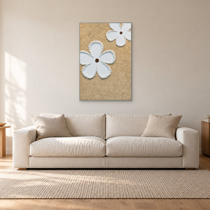 Tableau vertical de fleurs blanches en relief à fin cadre argenté, au-dessus d’un canapé blanc cassé