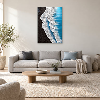 Tableau de vagues dans un cadre argenté, centré au-dessus d’un canapé clair aux coussins bleus et anthracite