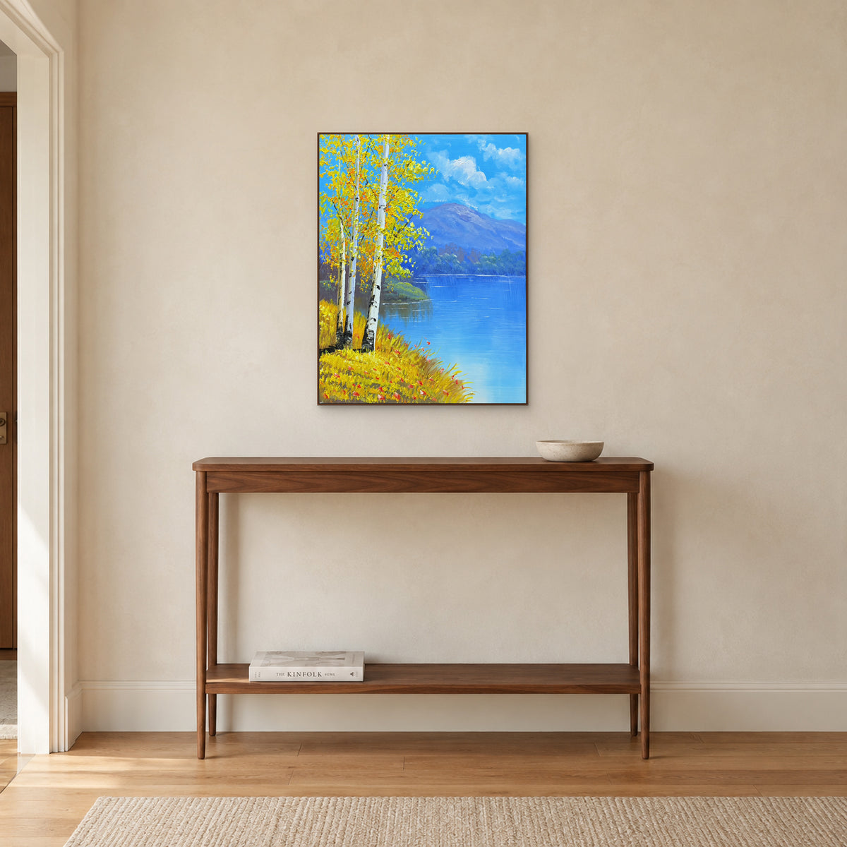 Tableau de rive bordée de bouleaux dans un cadre ton noyer au-dessus d’une console étroite en bois.