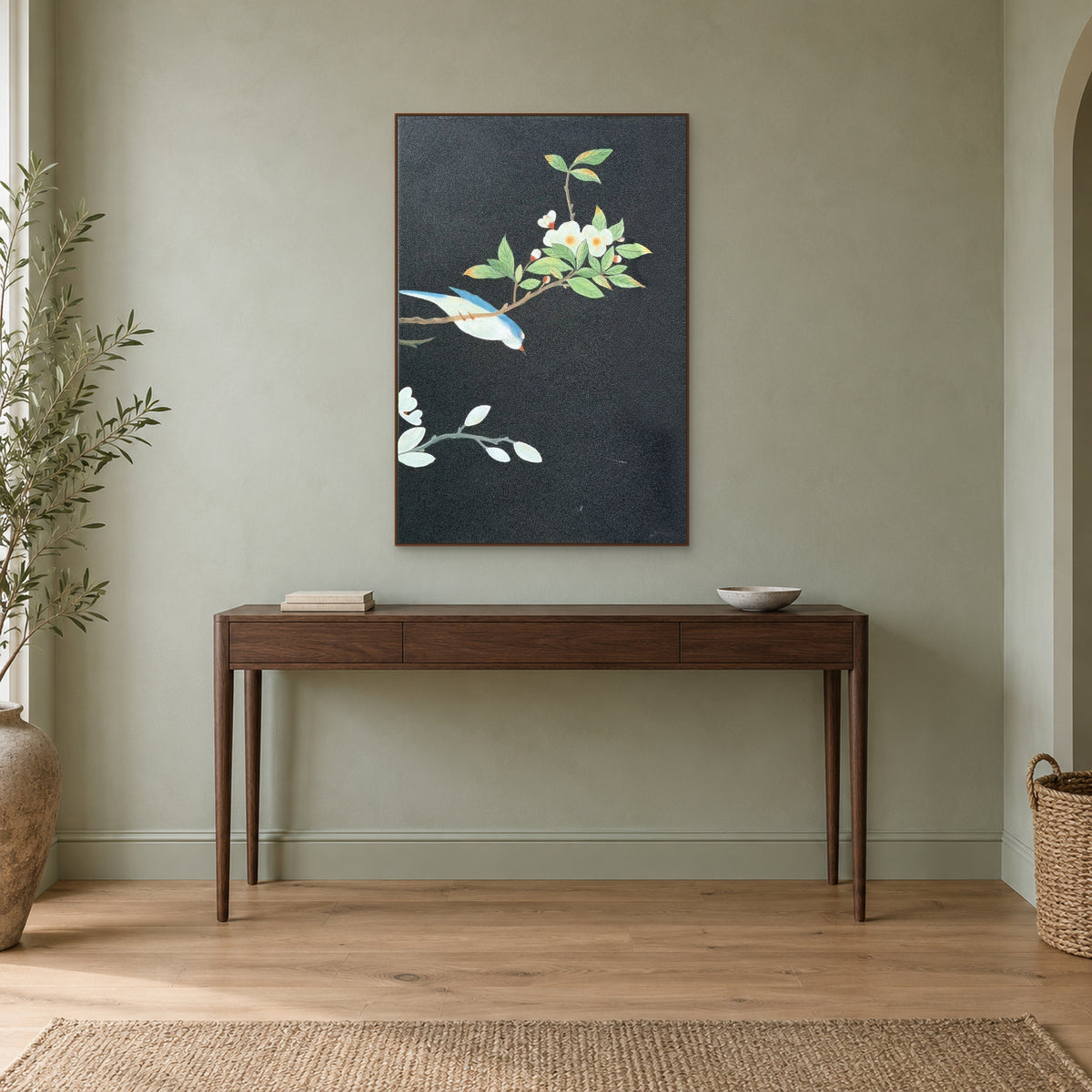 Fleurs blanches et oiseau bleu dans un cadre ton noyer, au-dessus d’une console fine sur un mur sauge