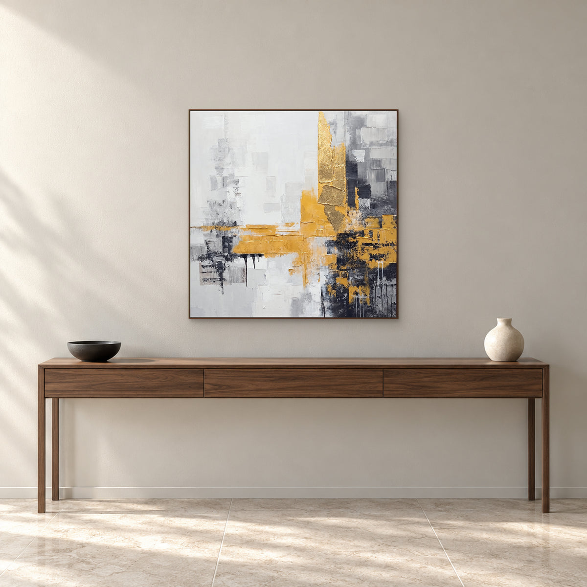 Tableau carré gris et doré dans un cadre ton noyer au-dessus d’une console en noyer avec un bol noir et un vase crème