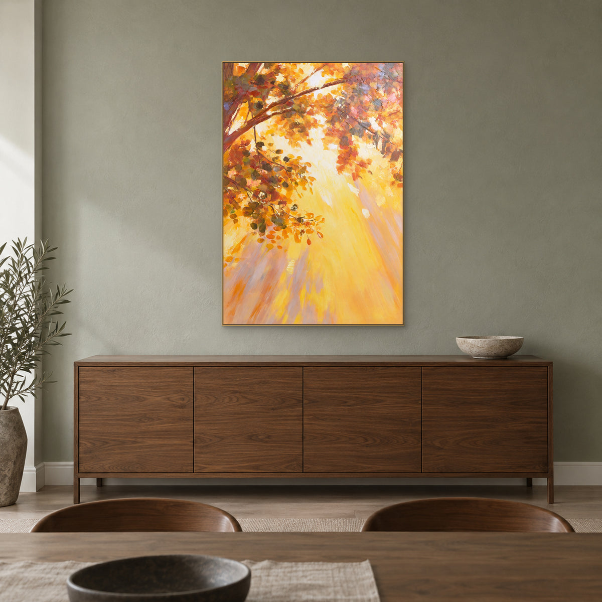 Tableau de feuillage doré dans un cadre flottant couleur champagne, au-dessus d’un buffet brun noyer dans une salle à manger.