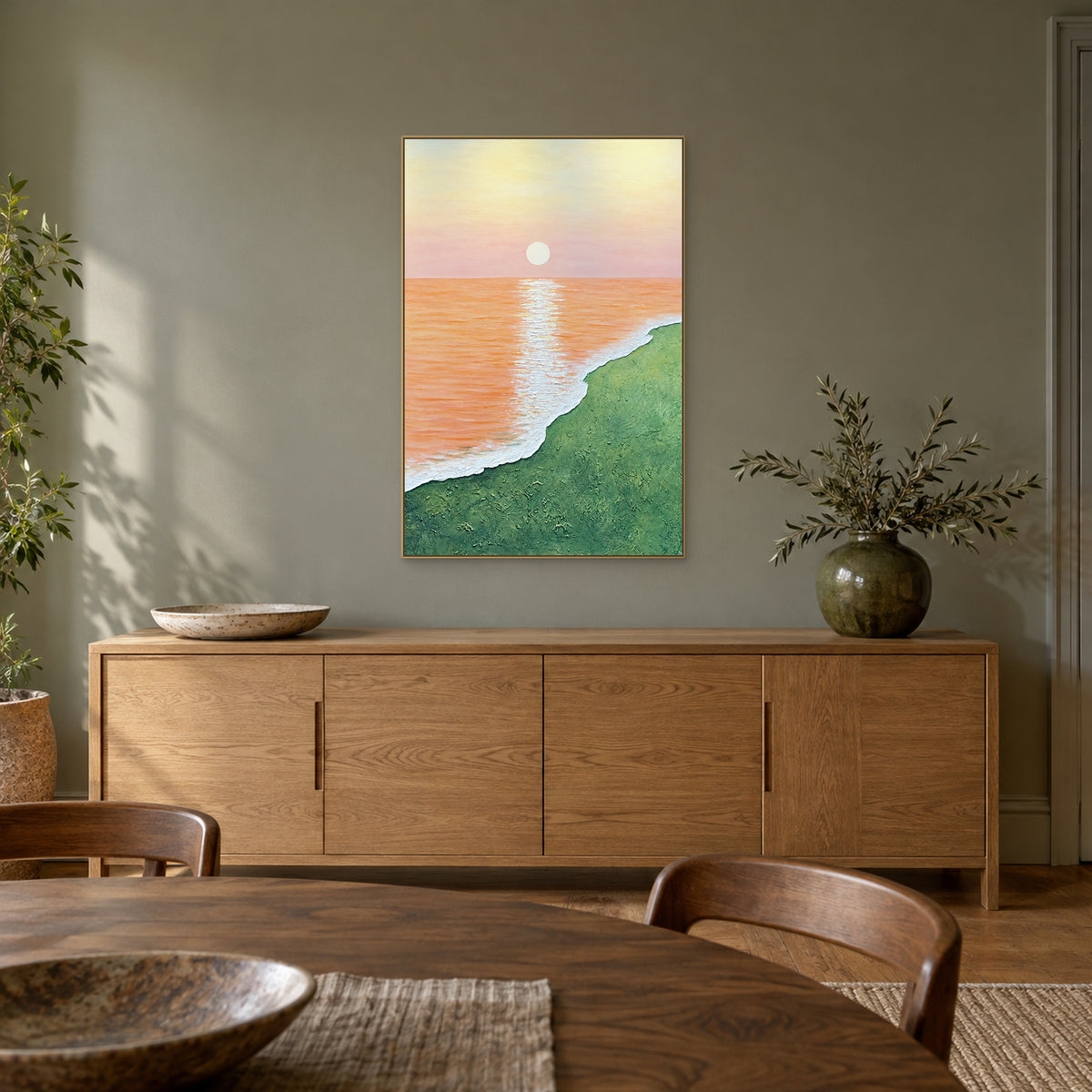 Tableau côtier abricot et vert dans un cadre champagne au-dessus d’un buffet en chêne, sur un mur vert