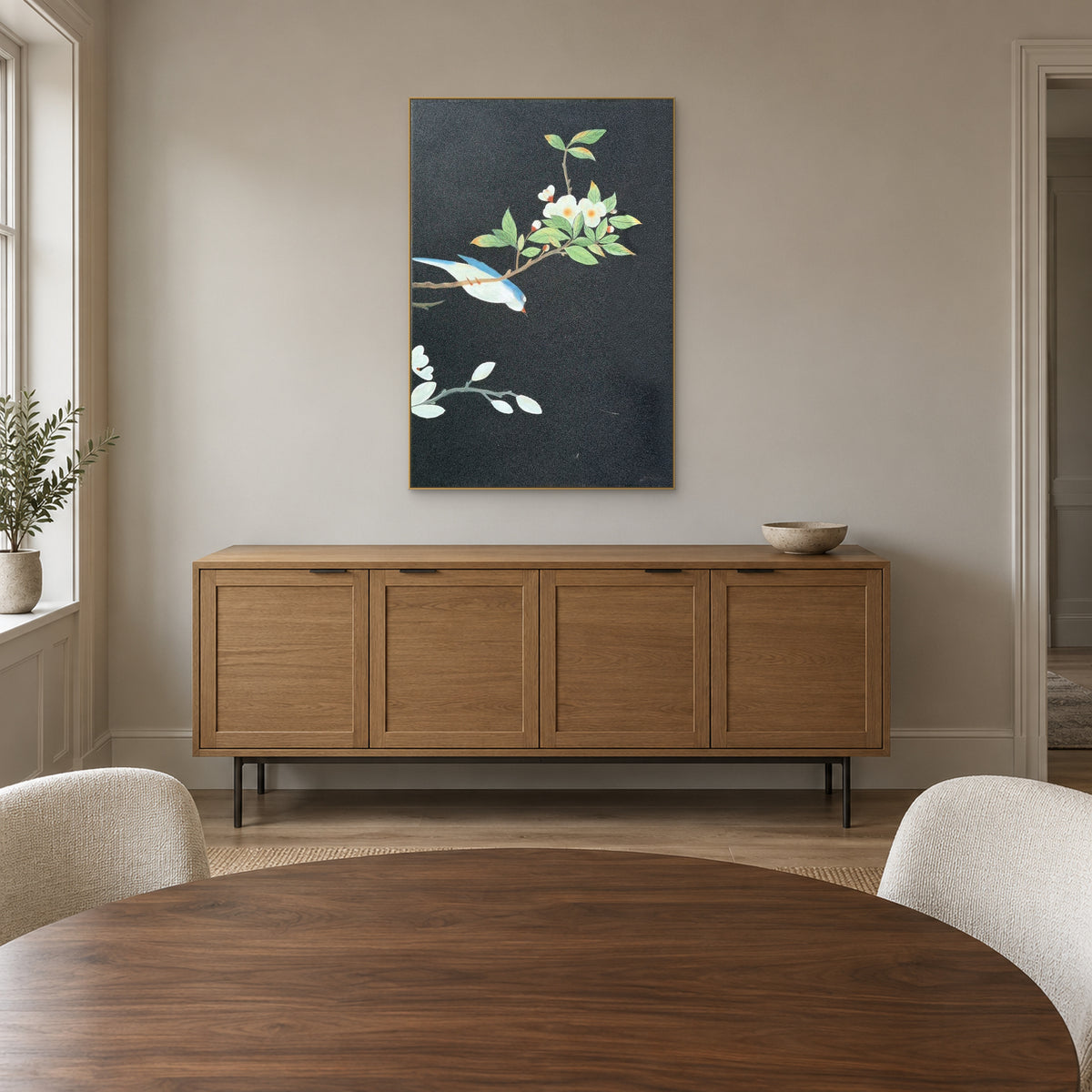 Tableau d’oiseau et de fleurs, cadre champagne au-dessus d’un buffet ton chêne, derrière une table ronde