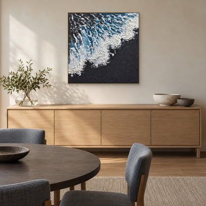 Square blue wave painting in a champagne-tone frame above an oak sideboard with a dining table in the foreground