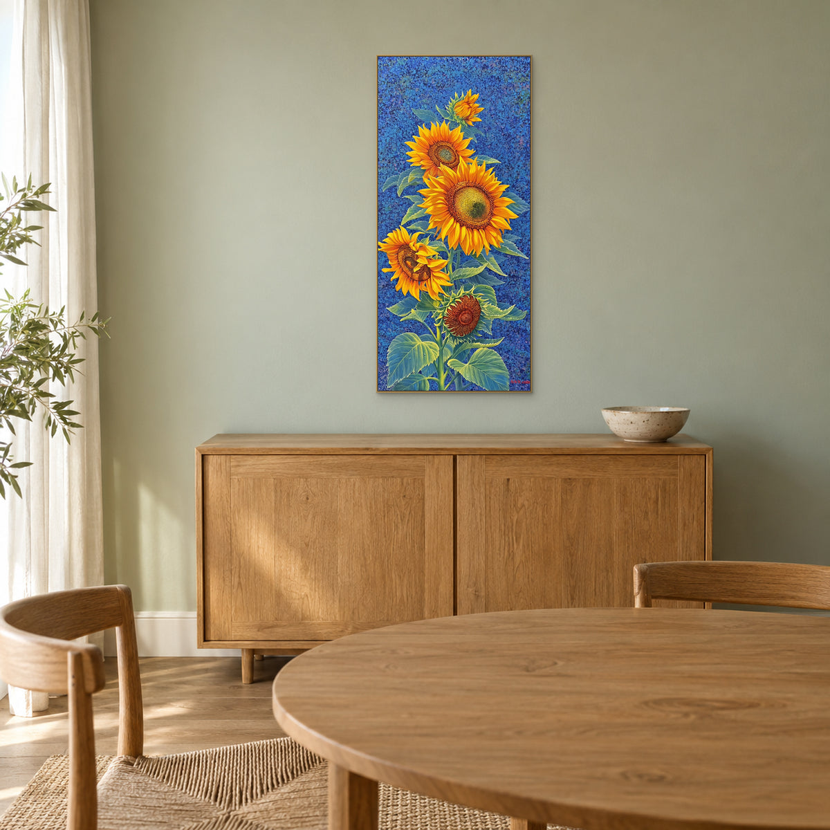 Tableau de tournesols dans un cadre champagne au-dessus d’un buffet en bois, sur un mur vert doux de salle à manger
