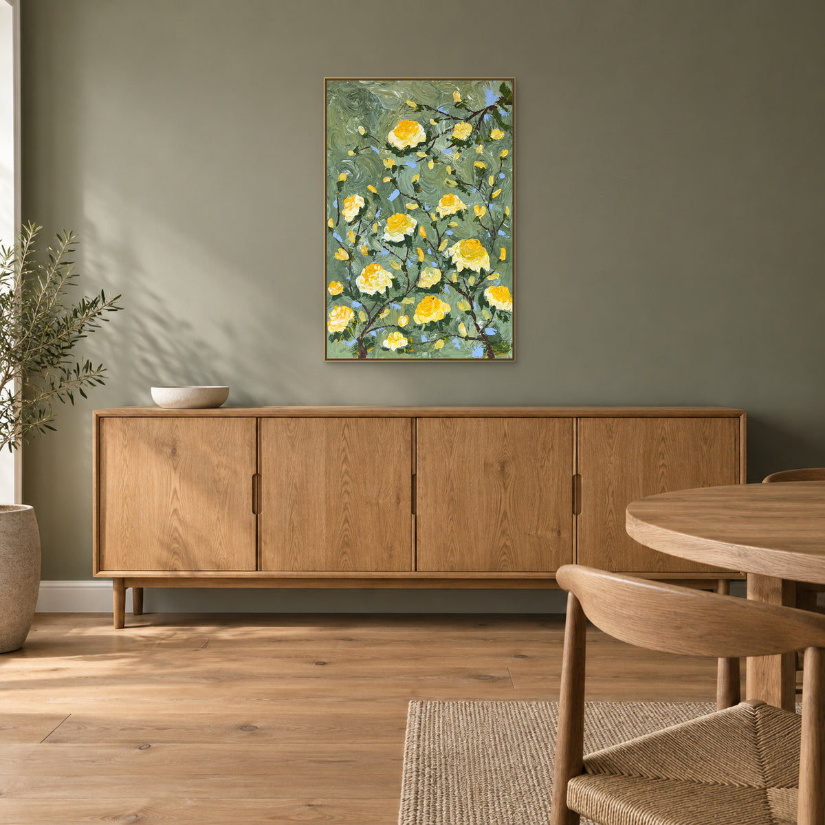 Yellow rose painting in a champagne-tone floating frame above an oak sideboard in a dining room