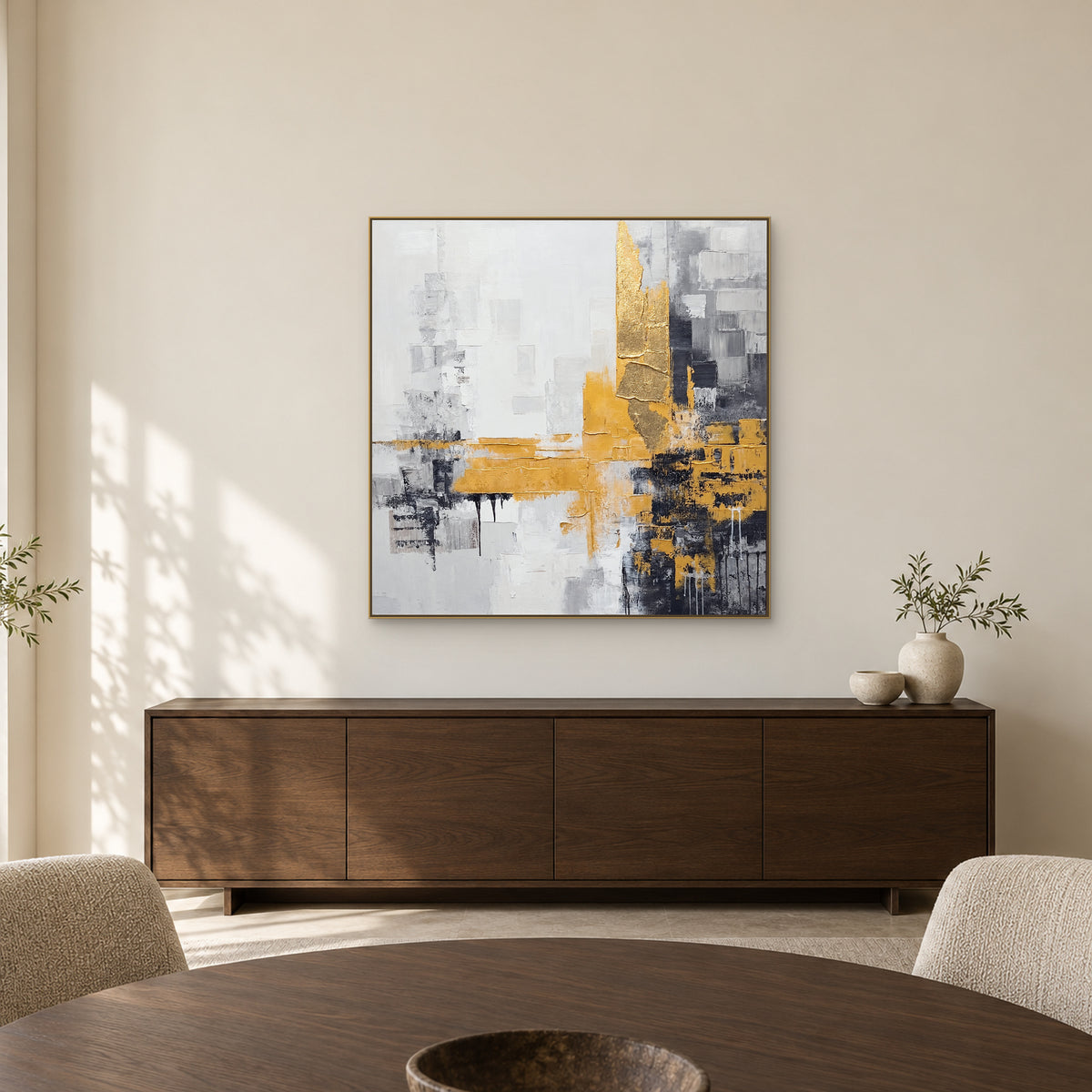 Tableau abstrait doré et charbon dans un cadre champagne au-dessus d’un buffet en chêne sombre, derrière une table ronde