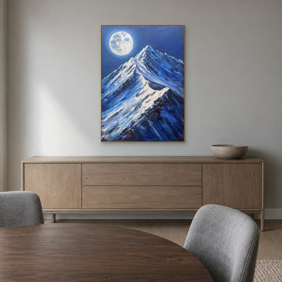 Peinture de montagne enneigée bleue dans un cadre champagne, au-dessus d’un buffet de salle à manger en bois