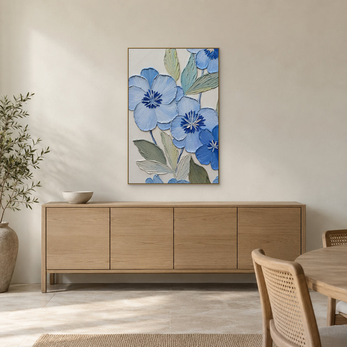 Fleurs bleues et feuillage sauge dans un cadre ton champagne au-dessus d'un buffet de salle à manger en bois clair