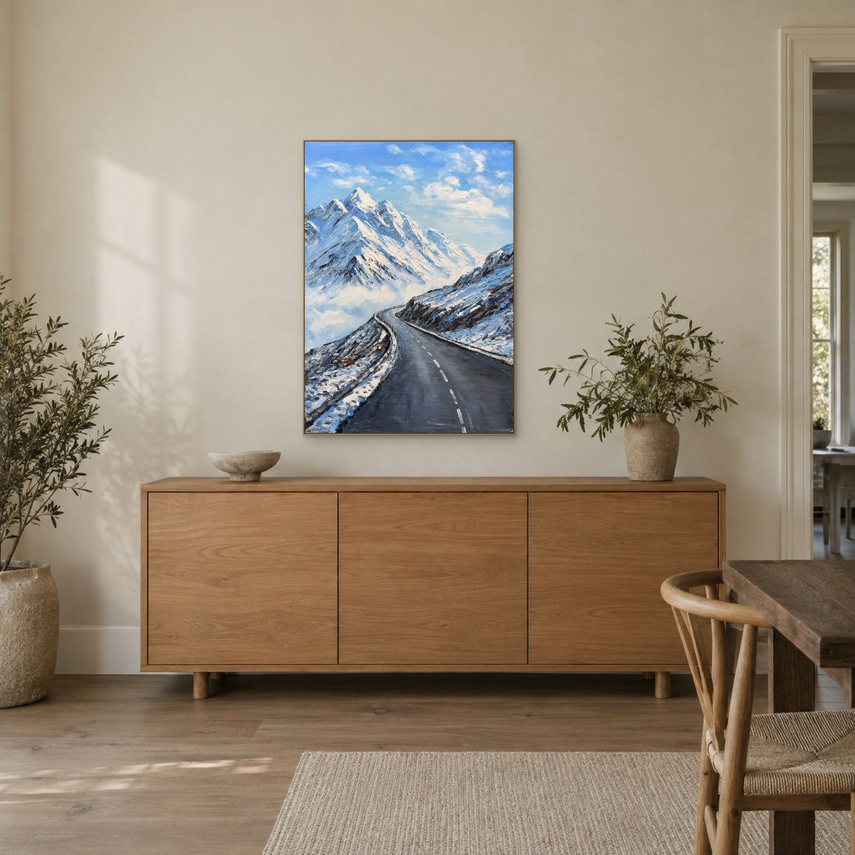 Tableau vertical de montagne enneigée, cadre flottant champagne, au-dessus d’un buffet en chêne près d’un vase feuillu